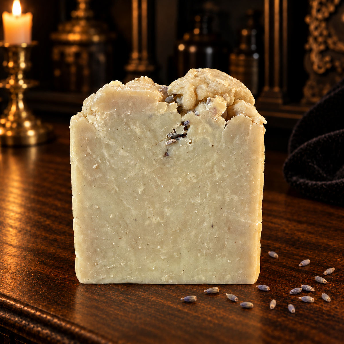 Cream-colored Lavender Moon soap with a textured top and loose dried lavender buds on dark wood.